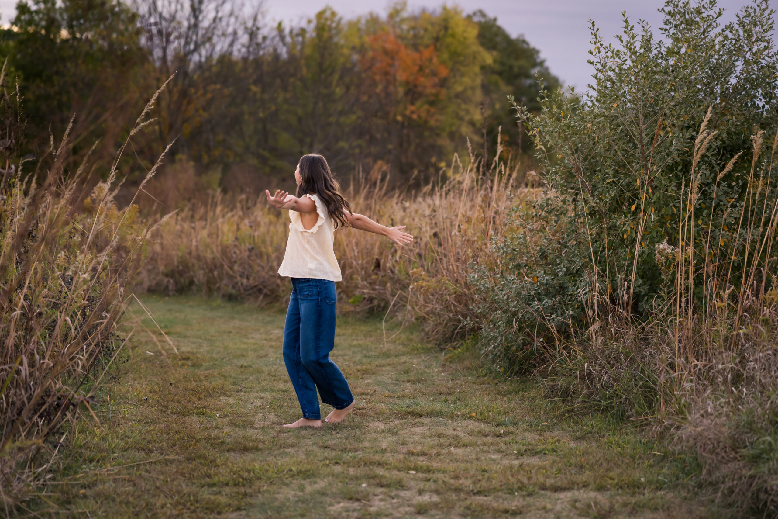 Candid senior portrait of young woman with arms outstretched in natural outdoor setting
